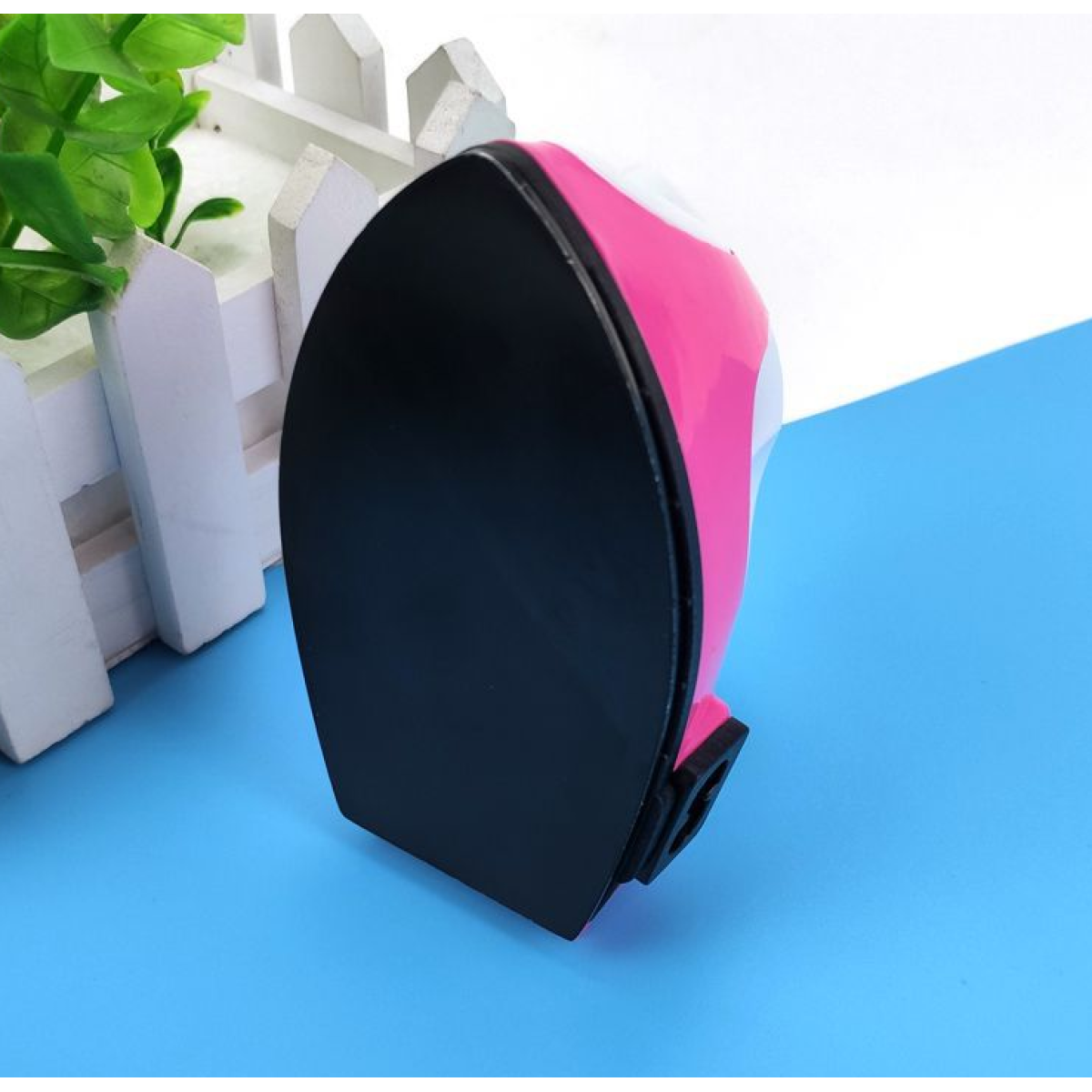 Ein Bügeleisen, schwarze Sohle, rosa und weißer Körper auf blauem Untergrund. Das Bügeleisen ist angewinkelt.