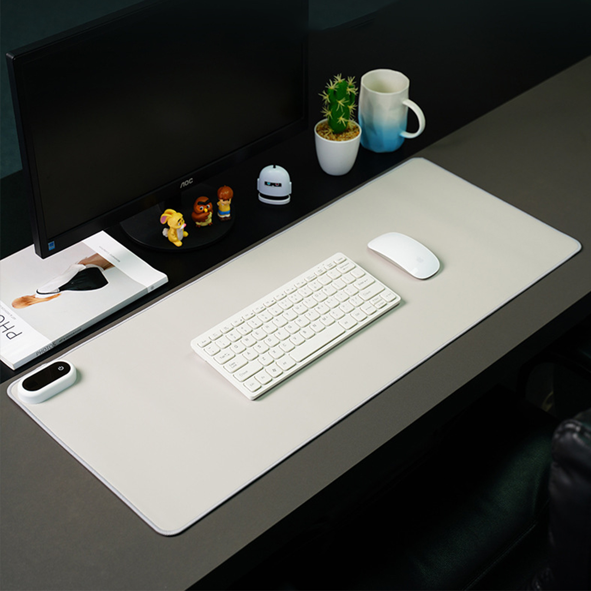 Ein Schreibtisch mit einem Computermonitor, einer Tastatur, einer Maus und einer Zeitschrift. Der Schreibtisch ist grau und der Hintergrund ist schwarz.