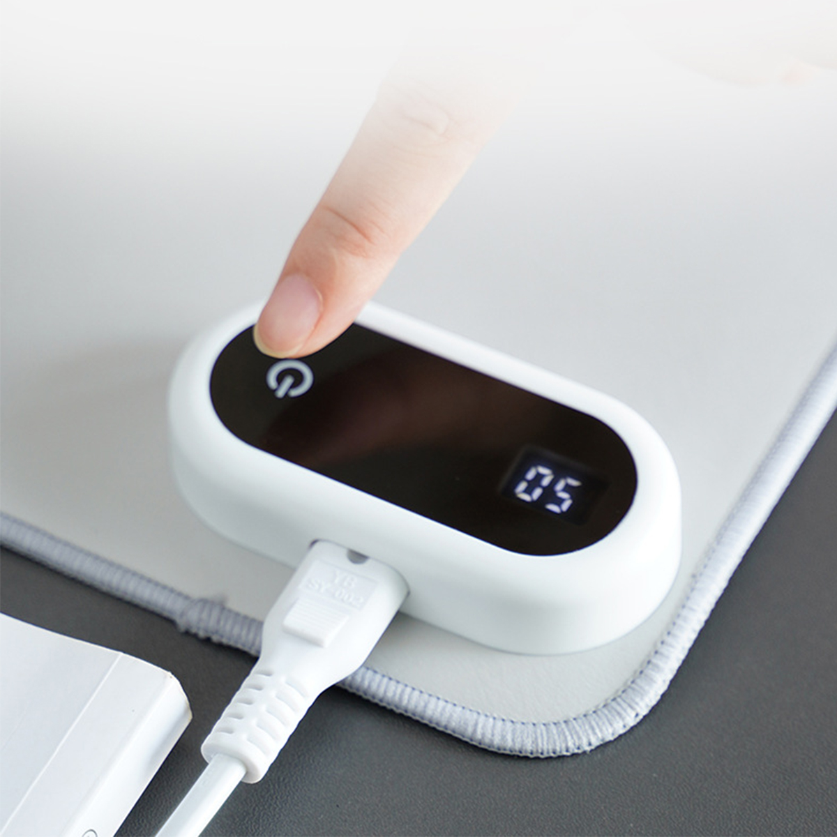 Ein Finger drückt einen Knopf auf einem weißen Ladepad mit digitaler Anzeige.