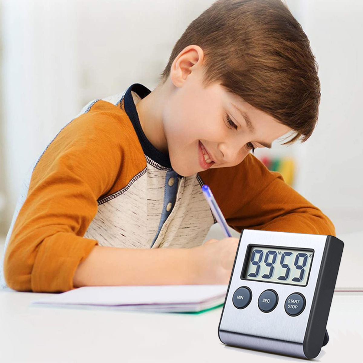 Ein Junge schreibt in ein Notizbuch, mit einem silber-schwarzen Timer im Vordergrund.