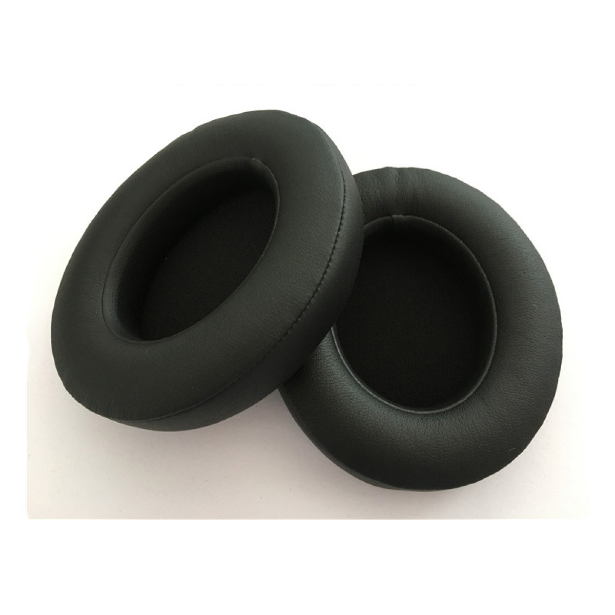 Dwie czarne, okrągłe nauszniki do słuchawek, leżące na białej powierzchni.