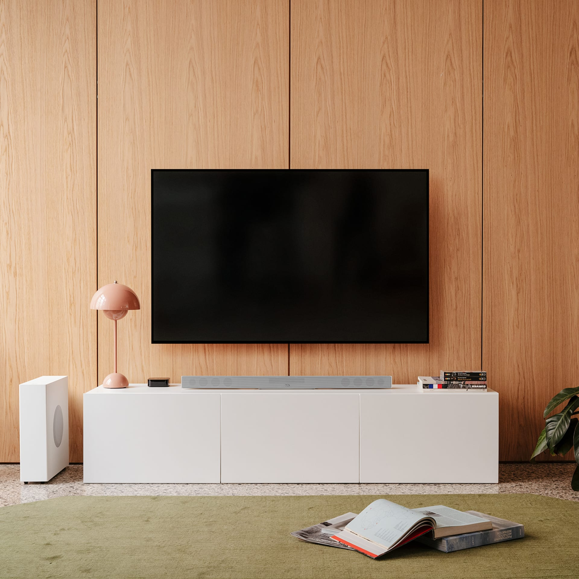 Modernes Wohnzimmer mit Fernseher, weißer Soundbar und grünem Teppich.