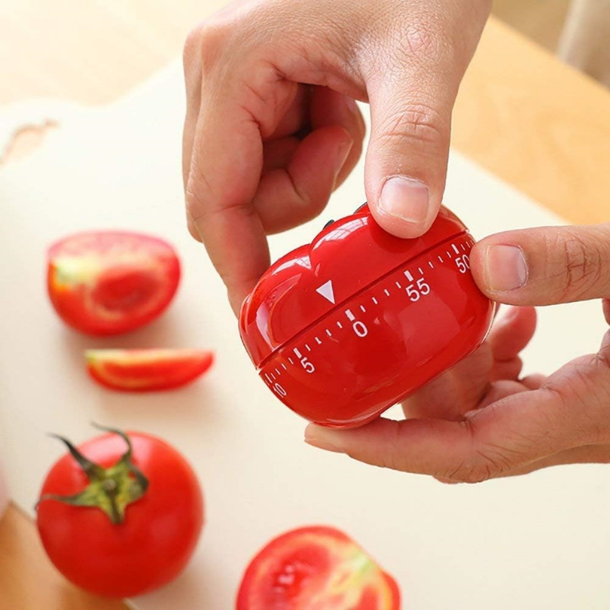 Roter Tomaten-Timer mit Tomaten und Tomatenscheiben auf einem Schneidebrett. Hände im Bild.