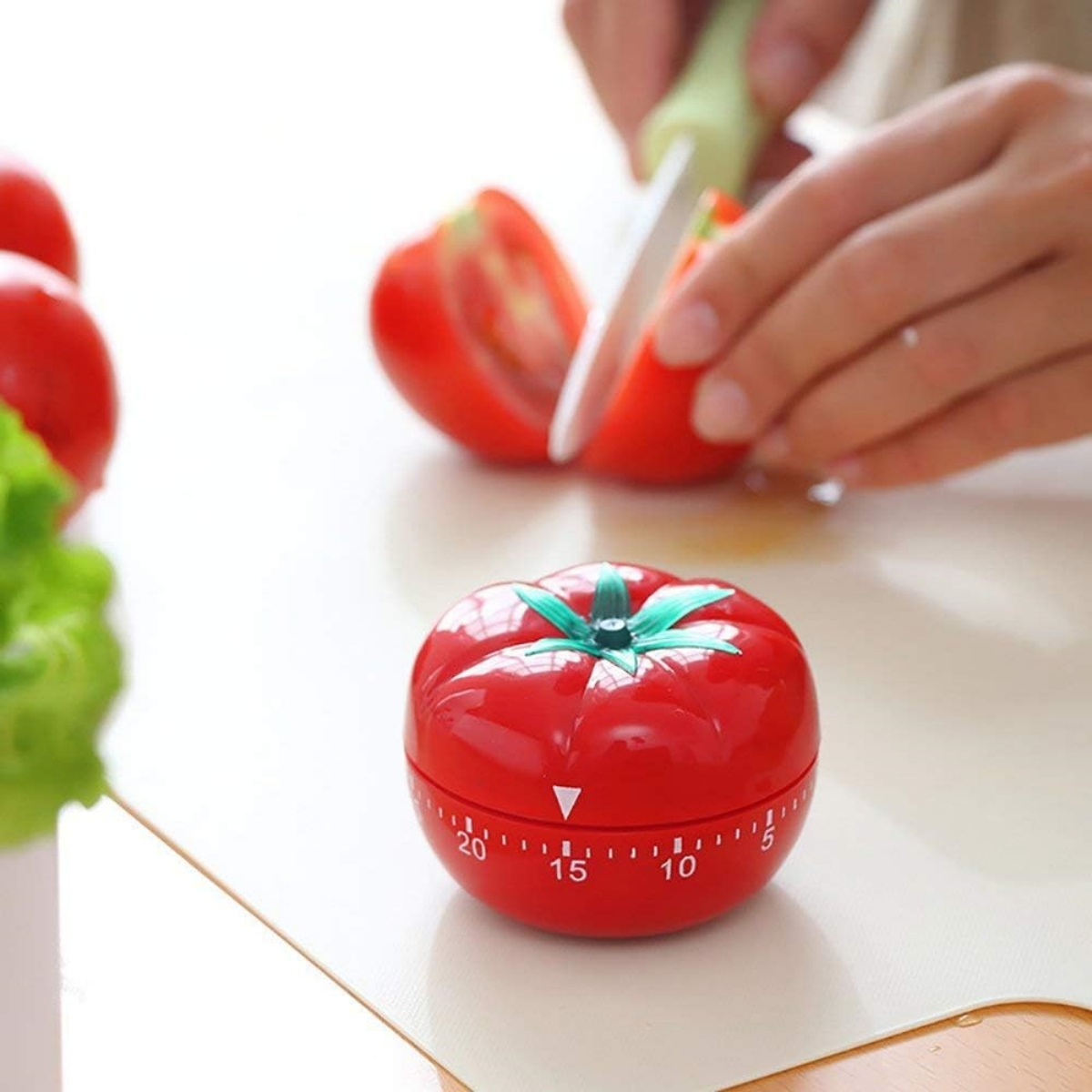 Tomatenförmiger Timer mit Händen, die eine Tomate auf weißer Oberfläche schneiden.