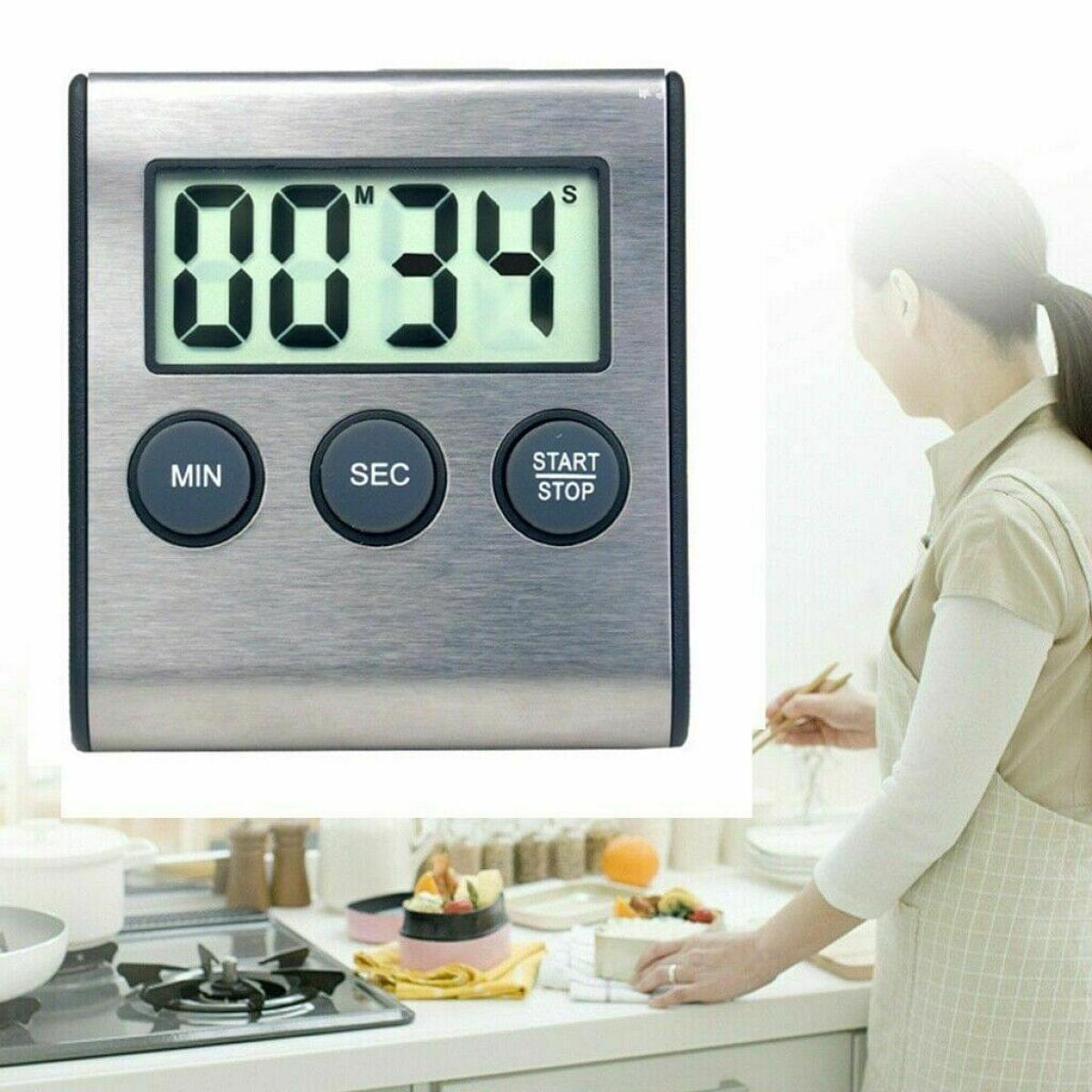 Ein silber-schwarzer Küchentimer mit digitaler Anzeige, die 00:34 anzeigt, und eine Frau im Hintergrund.
