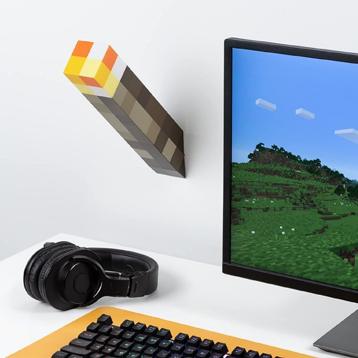 Eine Minecraft-Fackel an einer weißen Wand montiert. Der Hintergrund zeigt einen Monitor mit einer Minecraft-Szene und eine Tastatur.