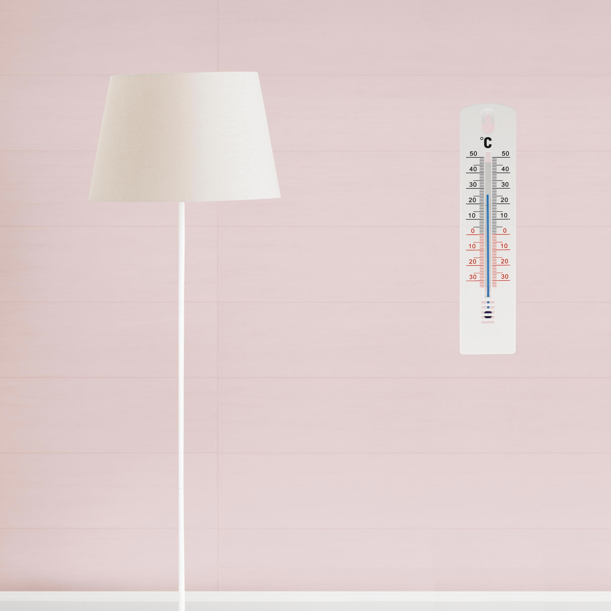 Eine Stehlampe und ein Thermometer an einer rosa Wand.