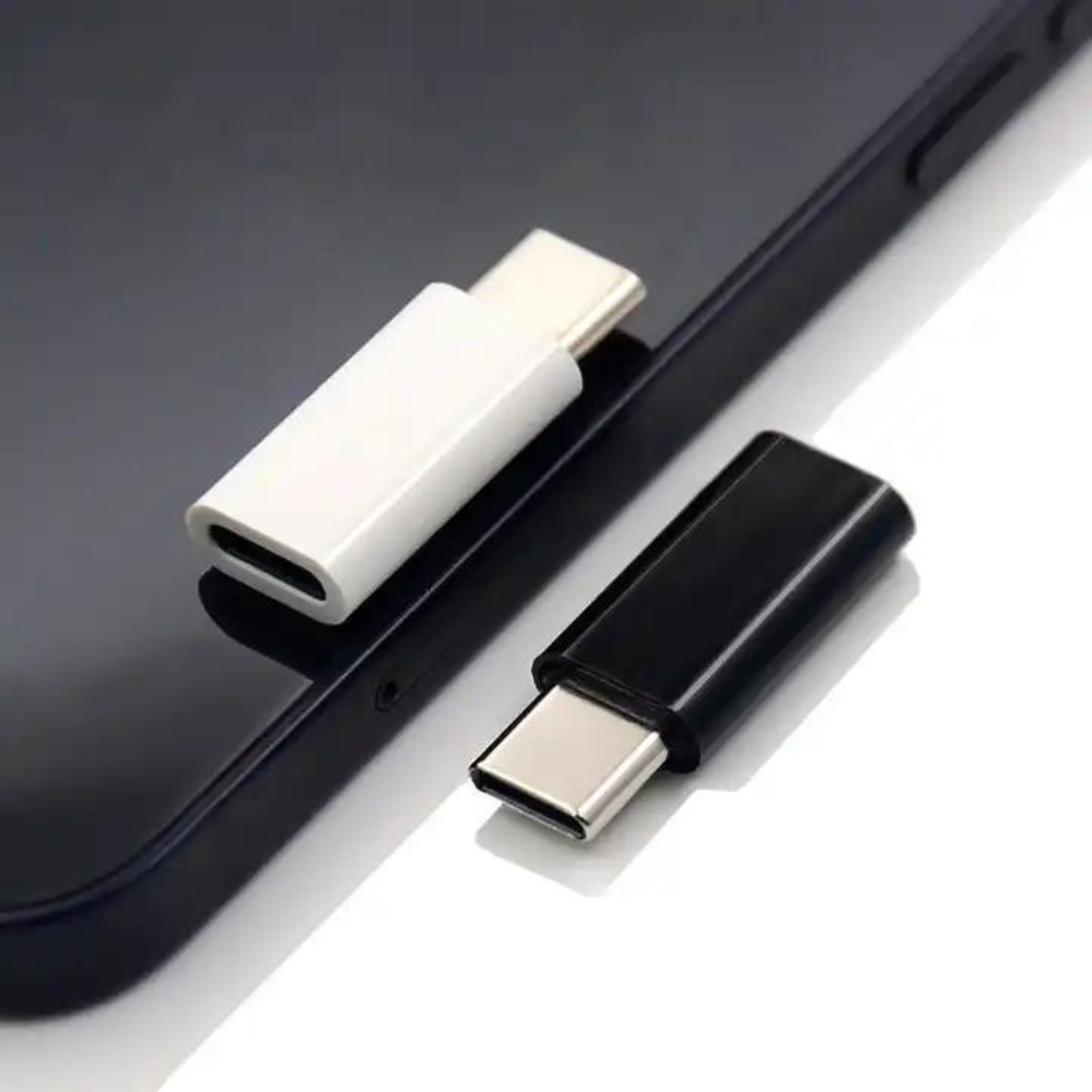 Zwei USB-C-Adapter, einer weiß und einer schwarz, liegen auf einem schwarzen Telefonbildschirm.
