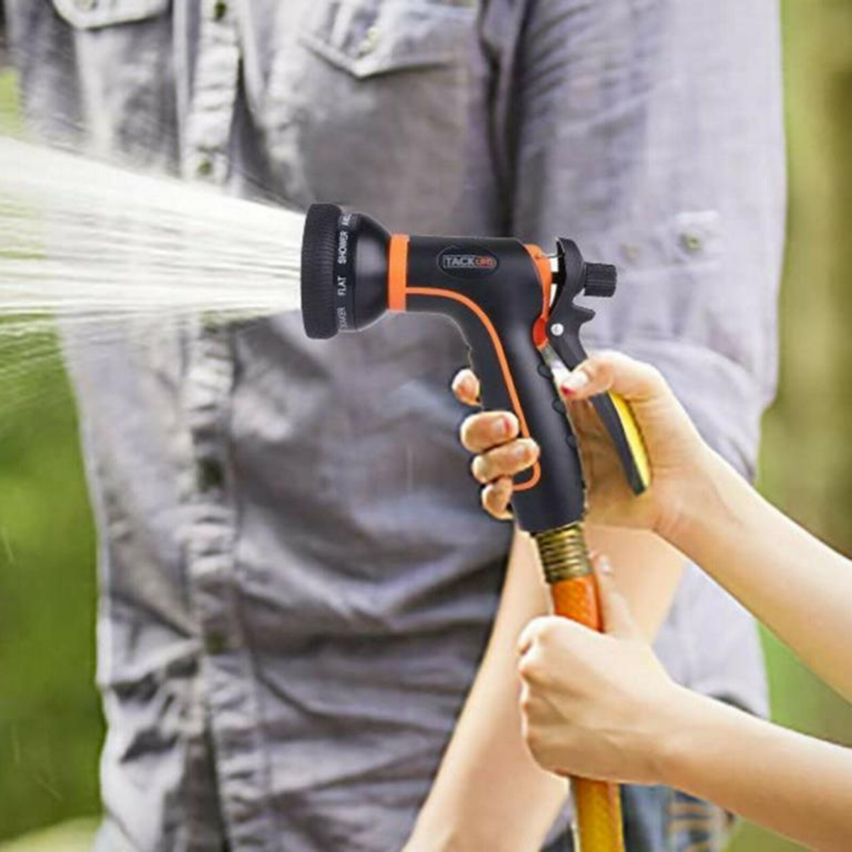Person sprüht Wasser aus einer Gartenschlauchdüse, gehalten von Händen einer Person.