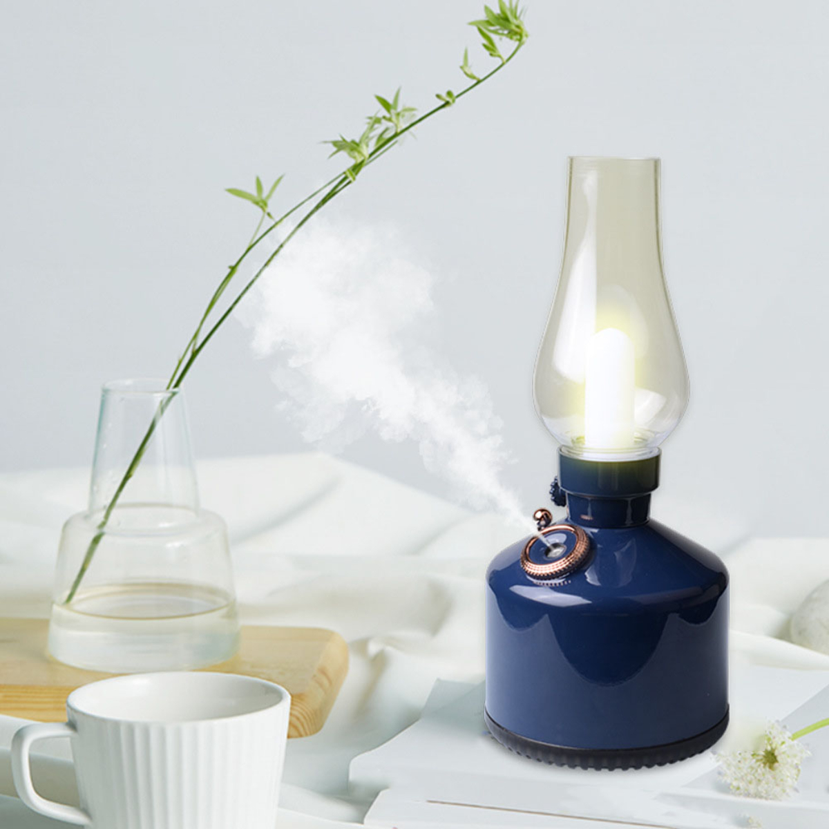 Eine blaue Lampe mit einer klaren Glühbirne sowie eine grüne Pflanze und eine weiße Tasse.