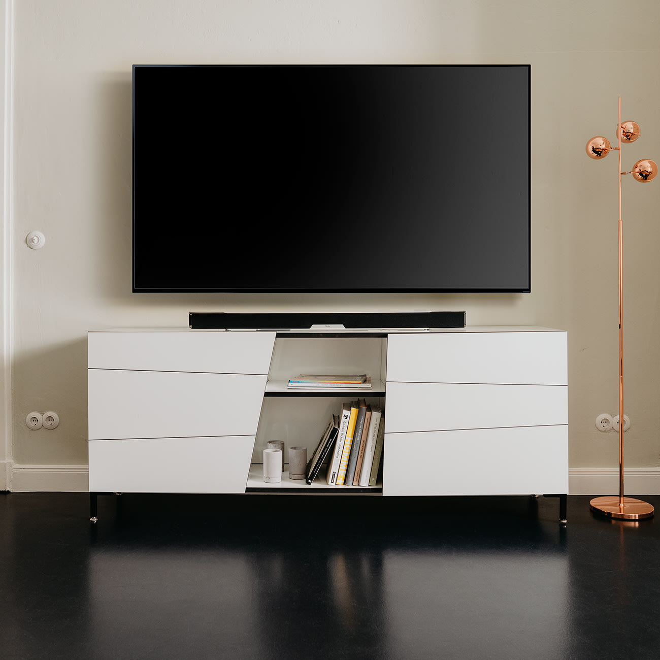 Ein Wohnzimmer mit einem großen Fernseher, einem weißen Schrank, einer Stehlampe und schwarzem Boden.