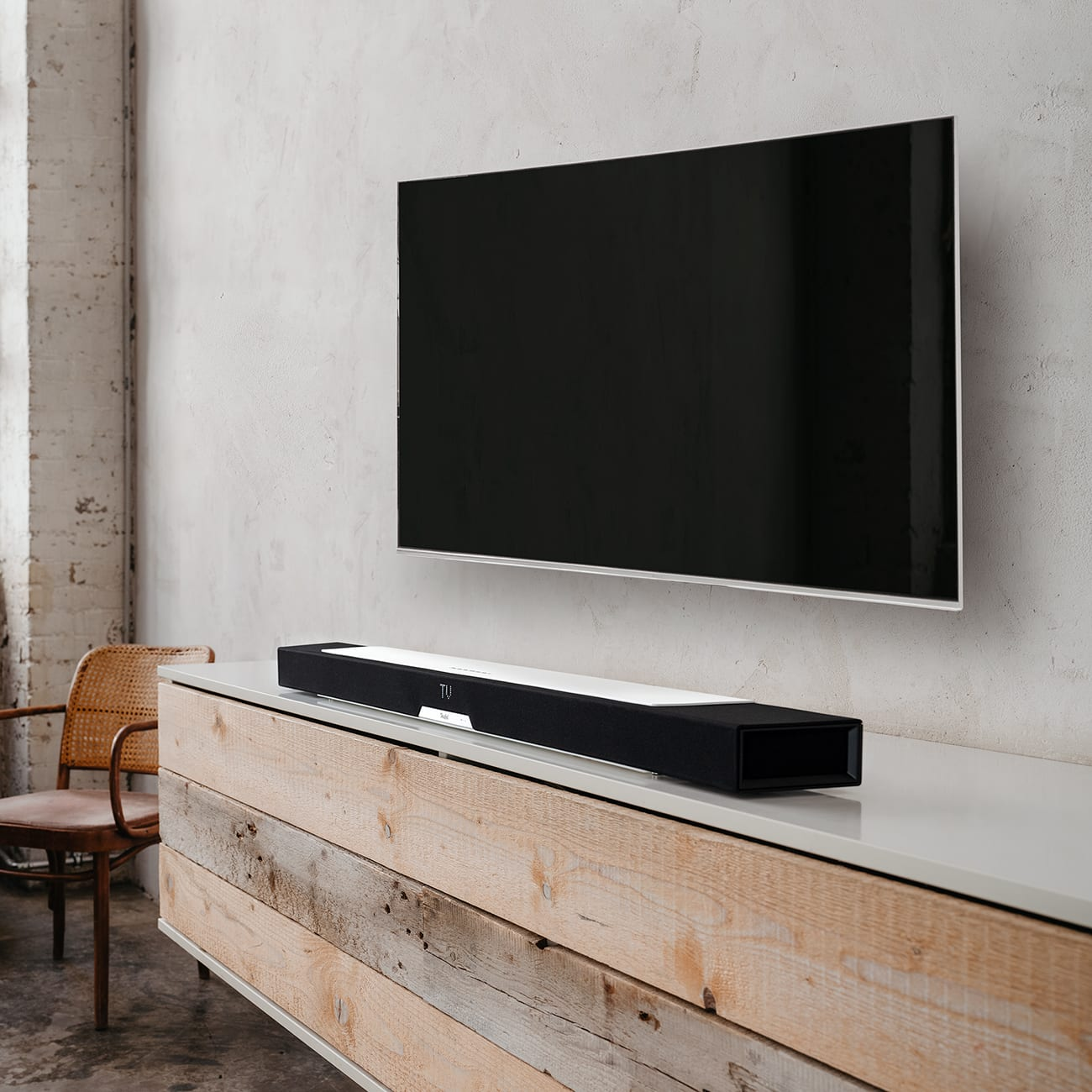 Ein Fernseher an der Wand über einem Holzschrank, mit einer Soundbar auf dem Schrank.