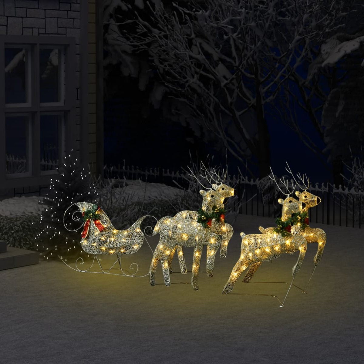 Leuchtende Rentier- und Schlitten-Weihnachtsdekorationen in einem verschneiten Garten bei Nacht.