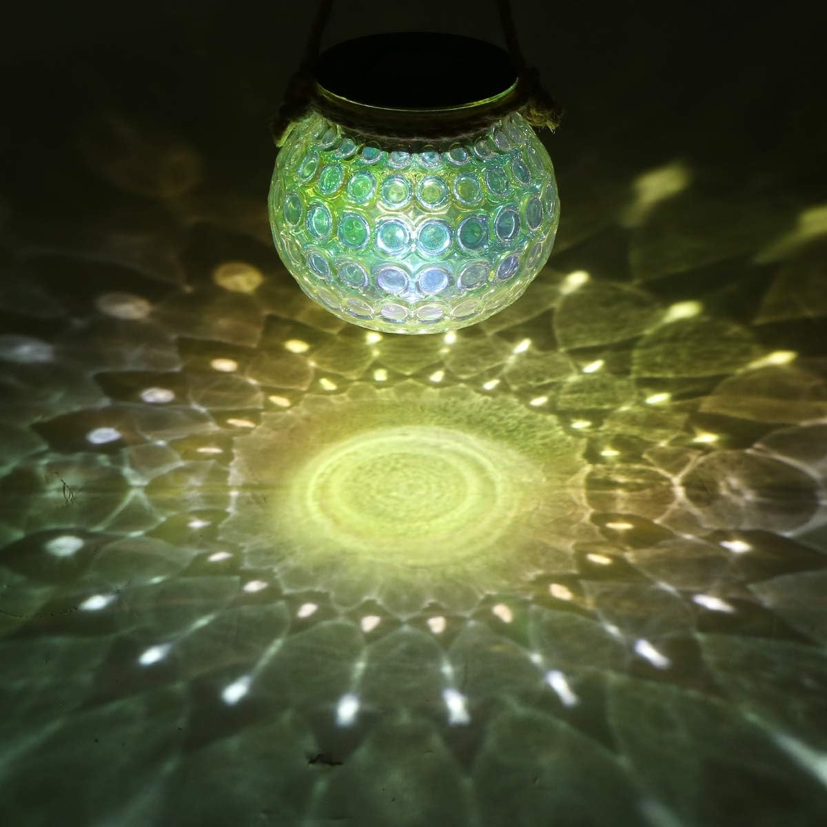 Eine leuchtende Glaskugellampe mit Seilgriff hängt und wirft ein Lichtmuster auf eine Oberfläche mit Grün- und Gelbtönen.