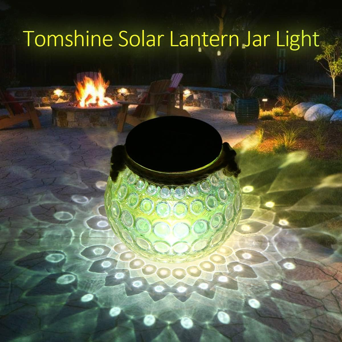 Eine Solar-Laterne beleuchtet eine Terrasse. Das Glas wirft Schattenmuster. Im Hintergrund befinden sich eine Feuerstelle und Sitzgelegenheiten.