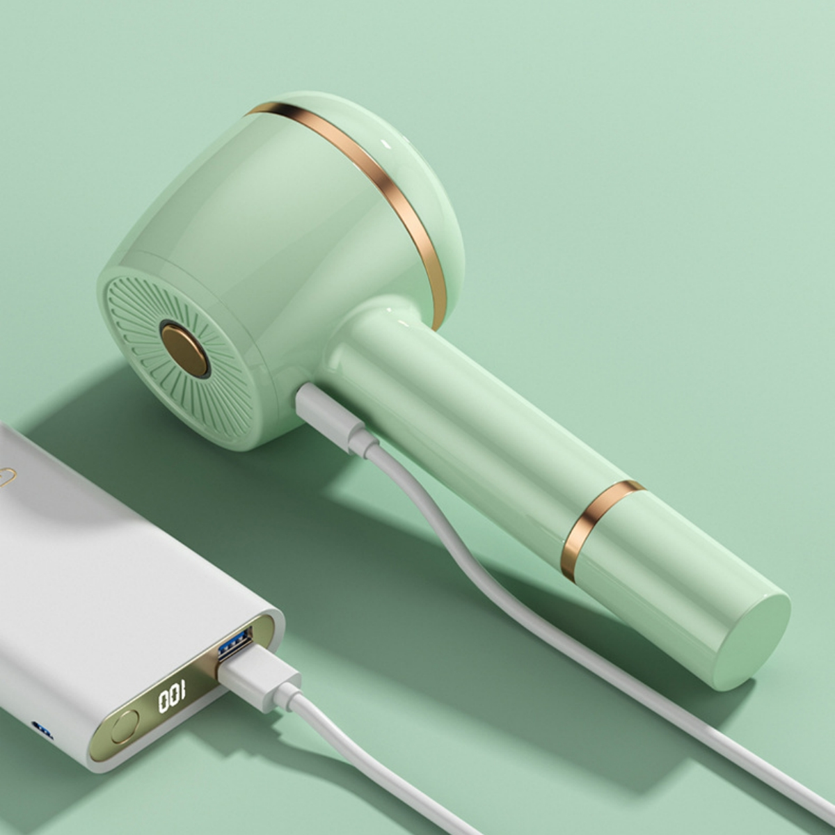 Minzgrüner Haartrockner, der von einer weißen Powerbank geladen wird. Goldakzente am Trockner. Weißes Kabel.