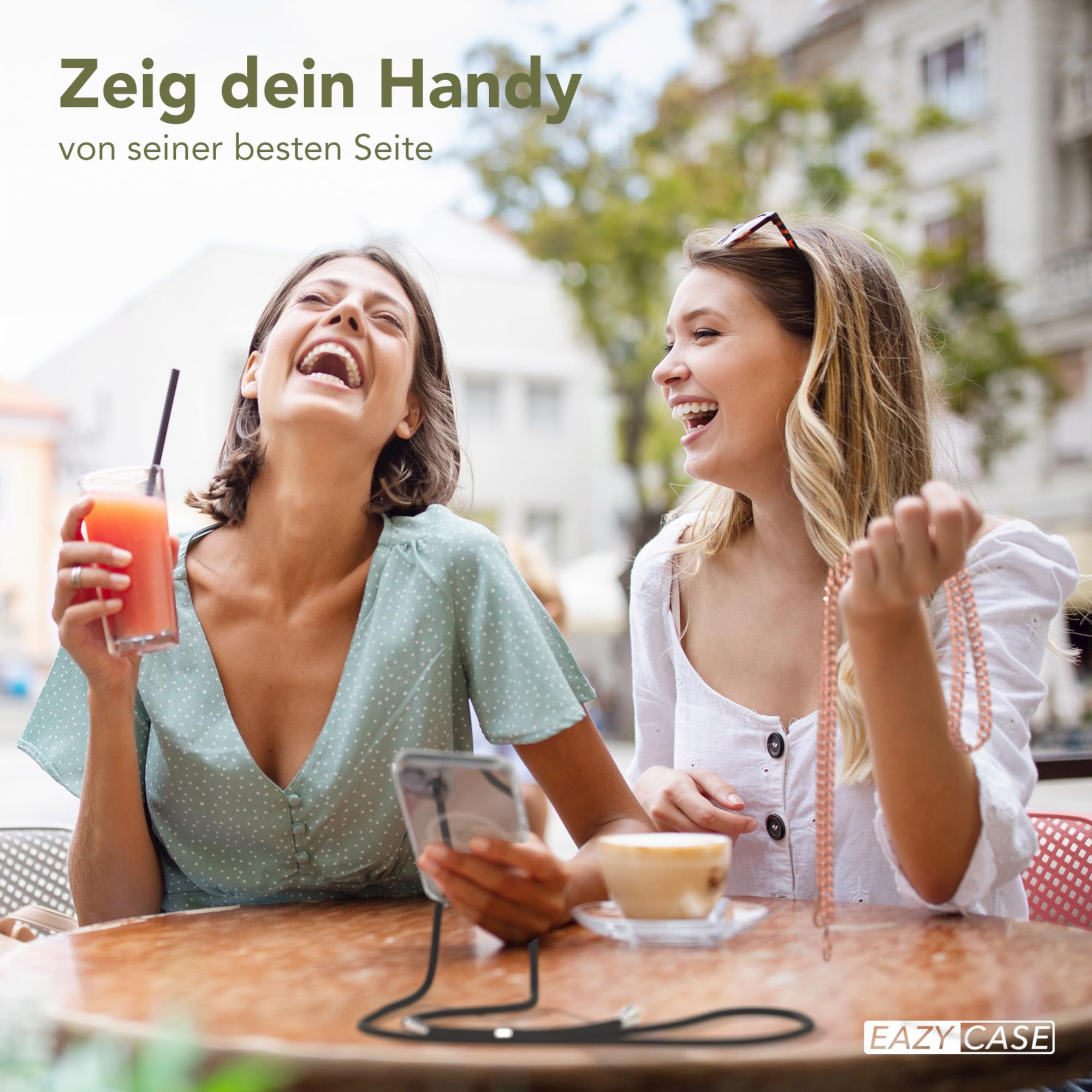 Zwei Frauen lachen und schauen auf ein Telefon mit schwarzem Kabel, sitzen an einem Tisch.