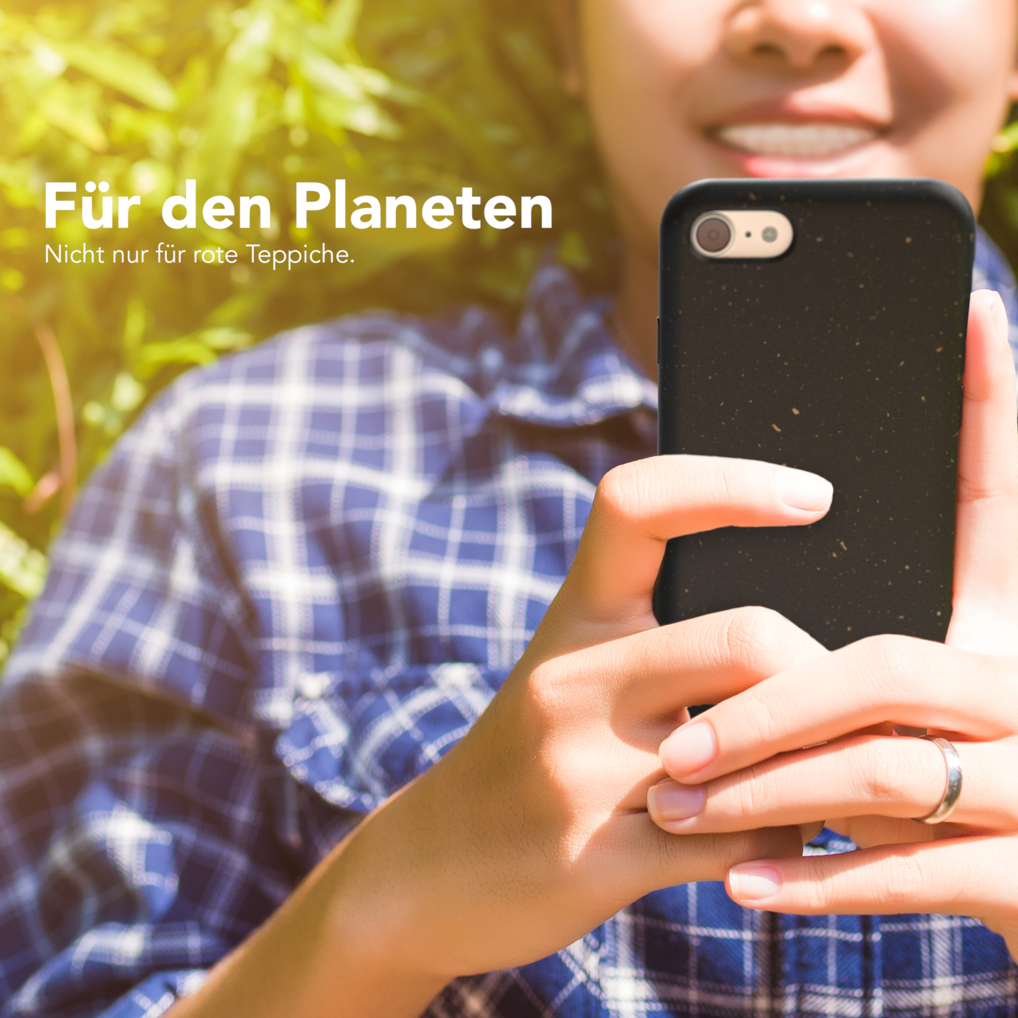 Eine Person hält ein Handy mit schwarzer Hülle. Grüne Blätter im Hintergrund.