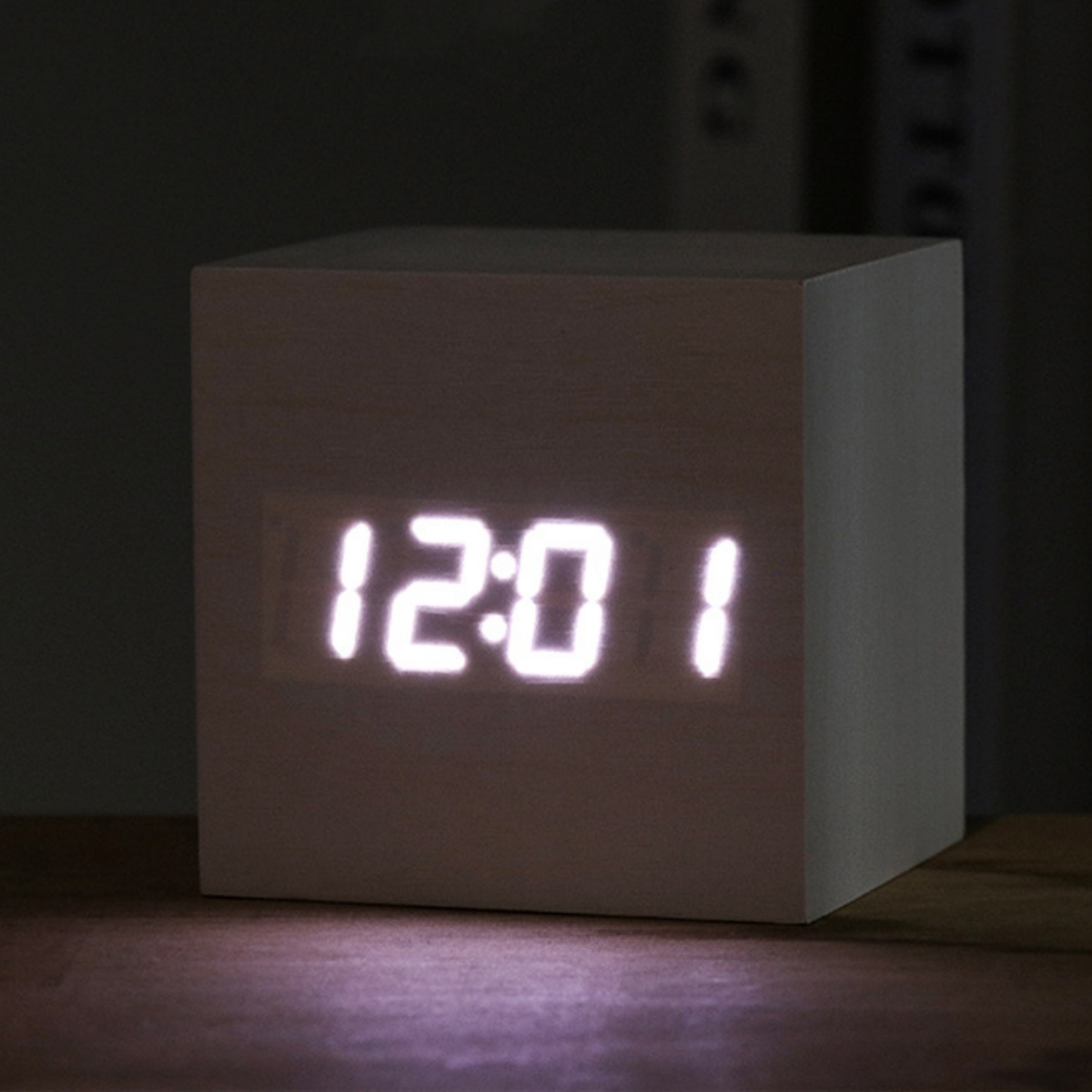 Digitaluhr im Holzquader-Design, 12:01 Uhr, auf Holzoberfläche beleuchtet.