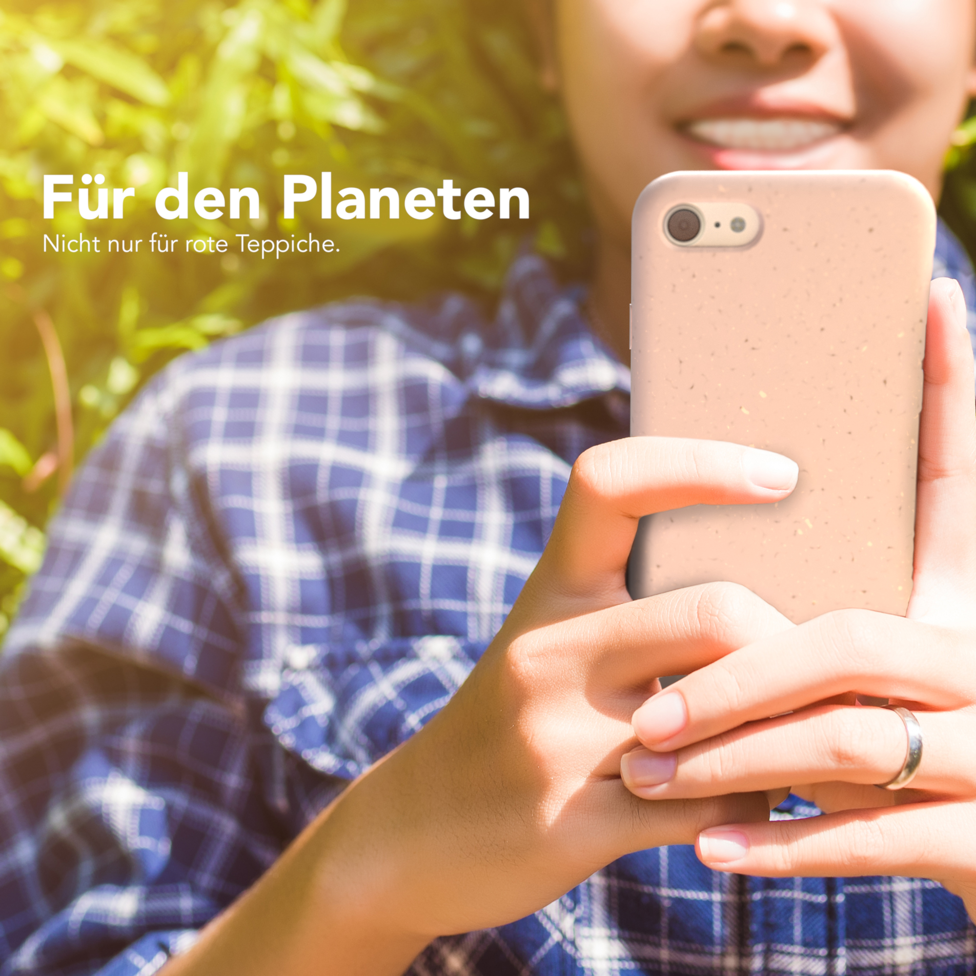 Person hält Telefon mit Hülle vor grünem Laub.