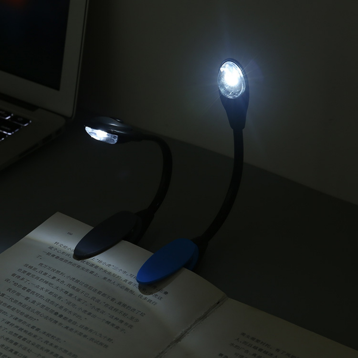 Zwei kleine schwarze LED-Lampen beleuchten ein Buch. Eine Lampe hat einen blauen Clip.