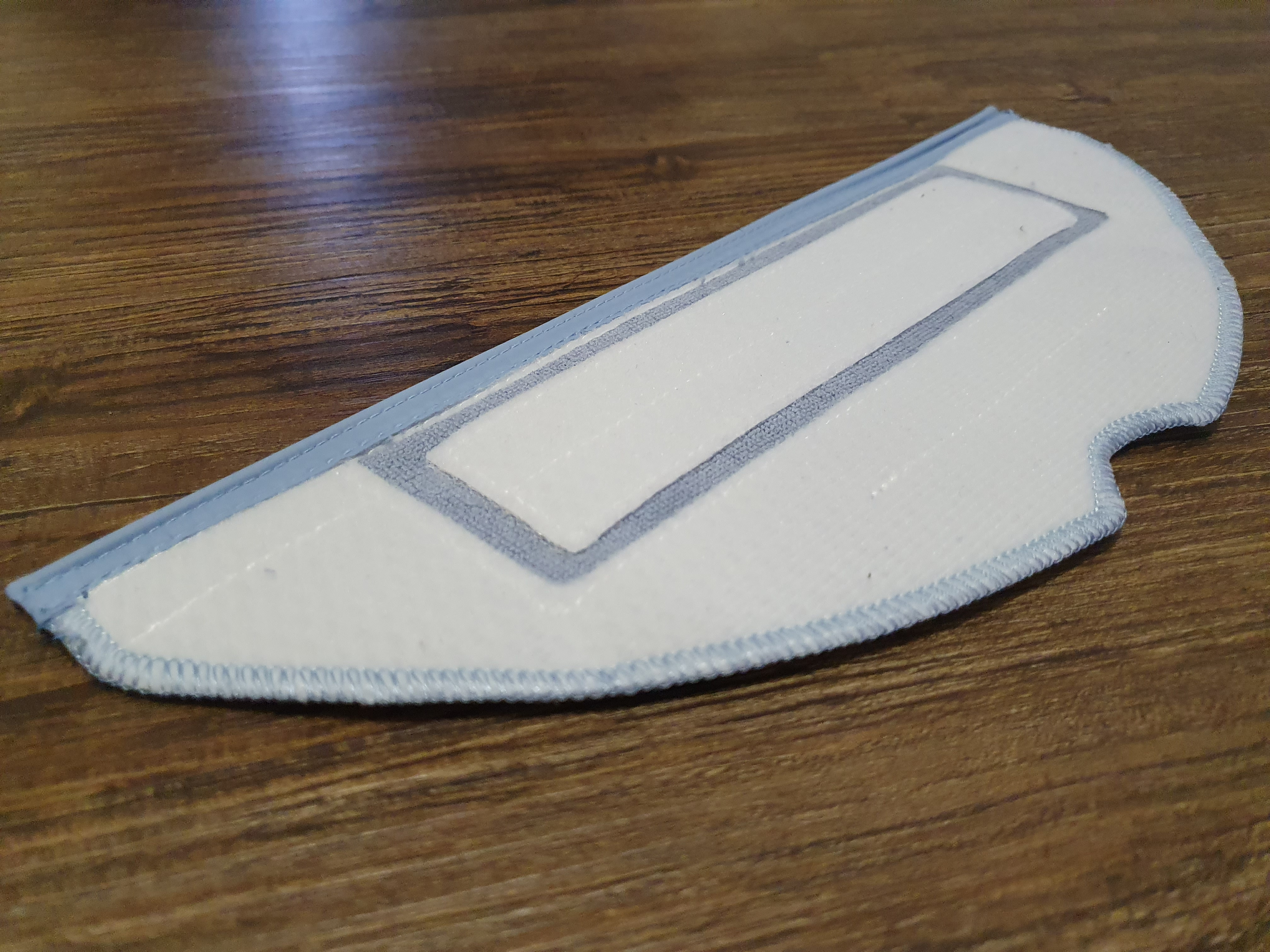 Weiß-blaues Reinigungspad auf Holzoberfläche. Rechteckige Form mit gebogener Seite.