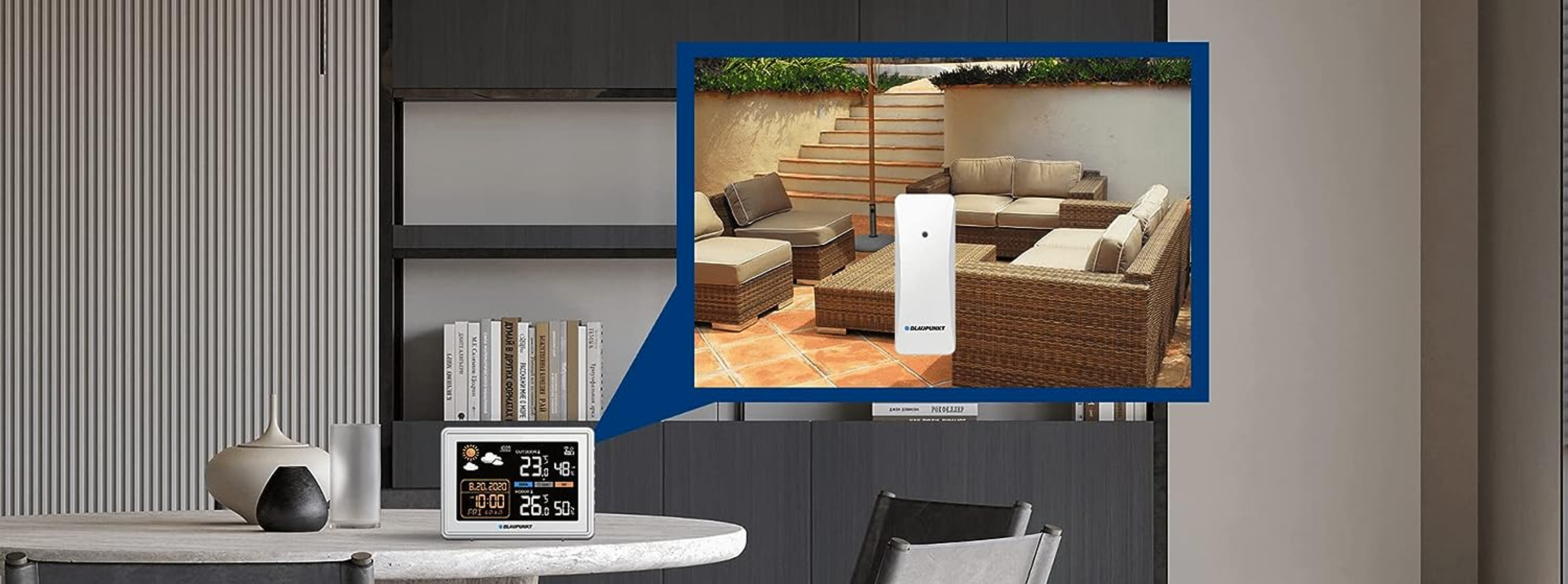 Eine Wetterstation auf einem Tisch mit verschwommenem Hintergrund, der eine Terrasse zeigt.
