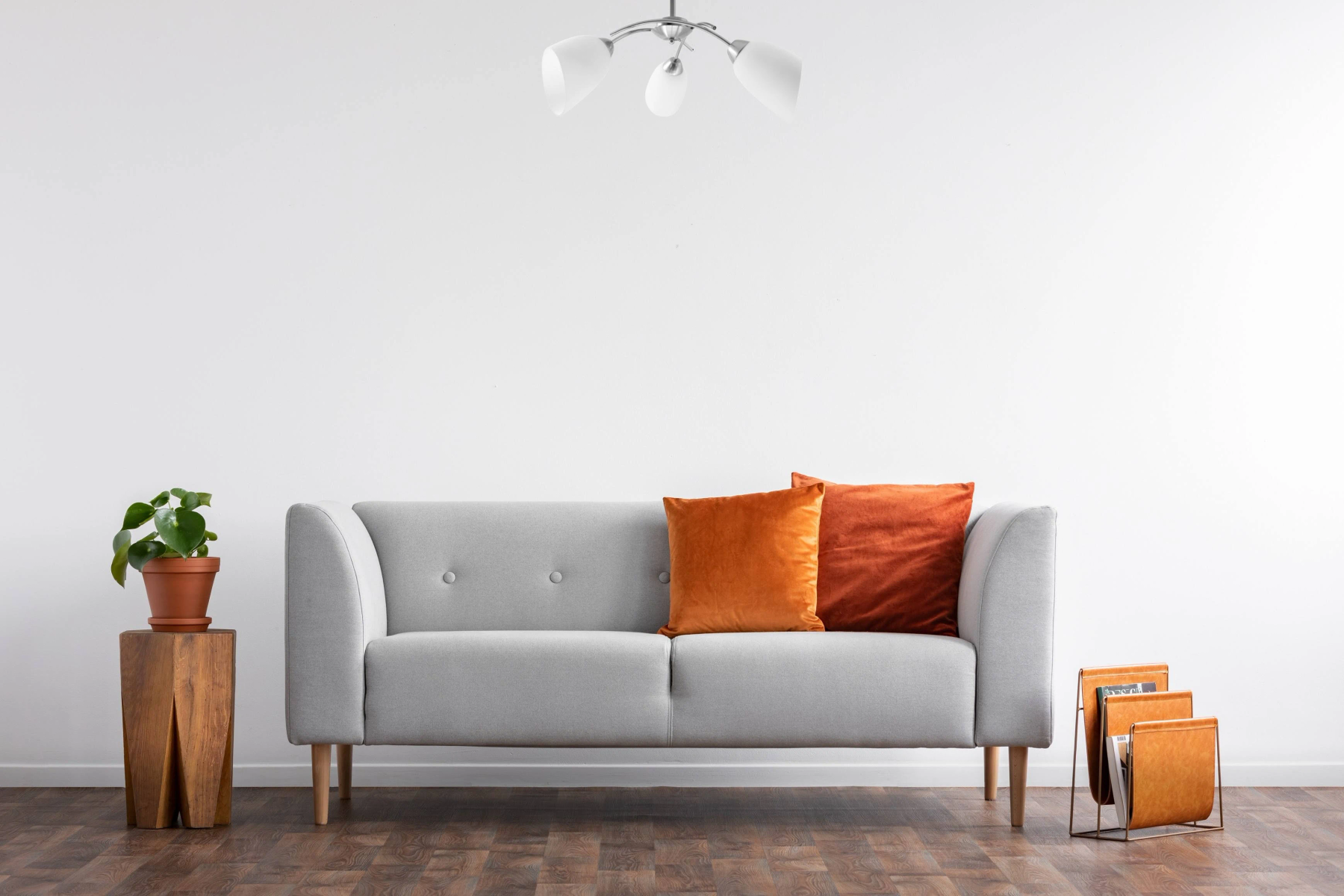Wohnzimmerszene mit grauem Sofa, orangefarbenen Kissen, Beistelltisch und Kronleuchter.