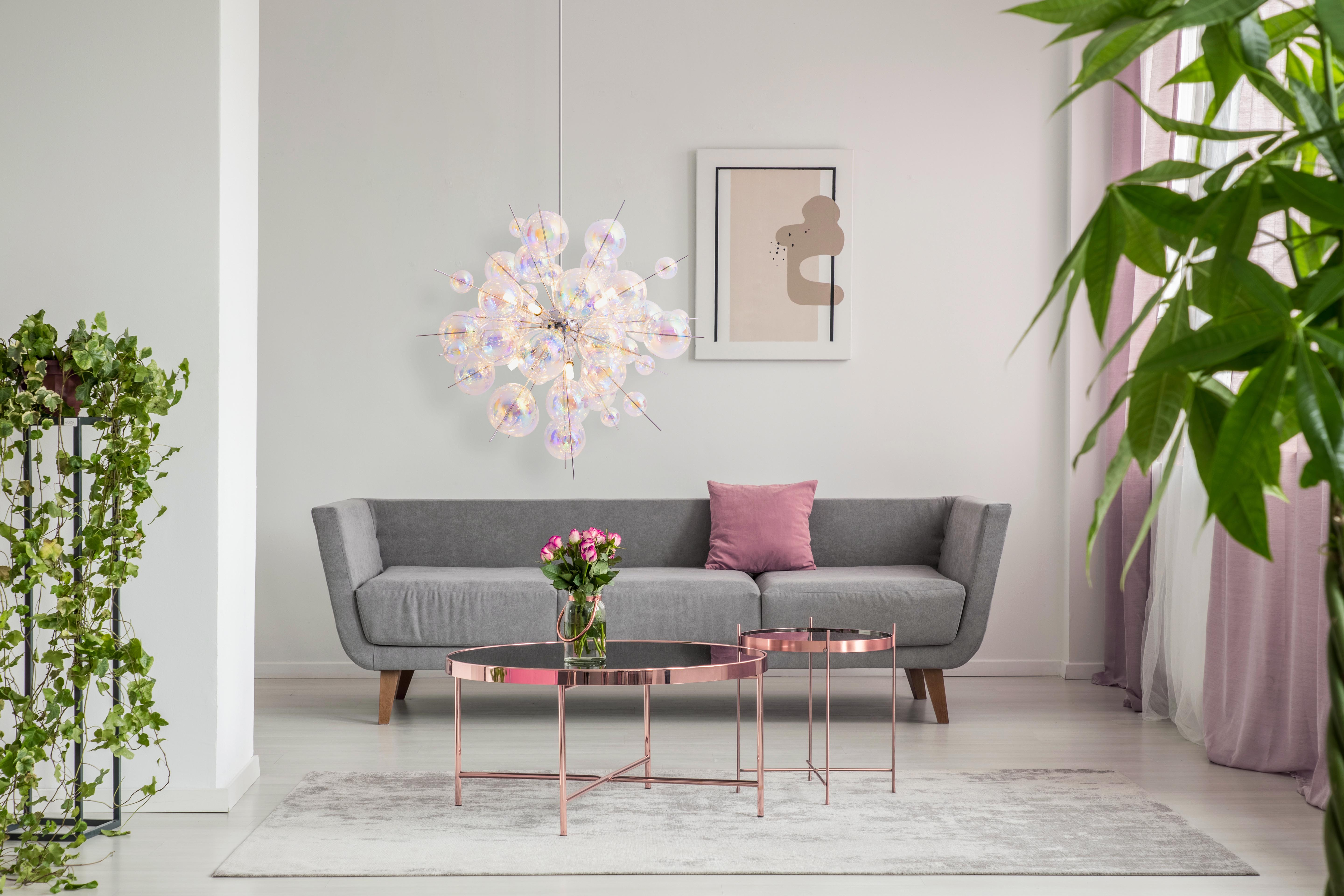 Innenaufnahme eines Wohnzimmers mit Sofa, Couchtischen und dekorativem Kronleuchter.