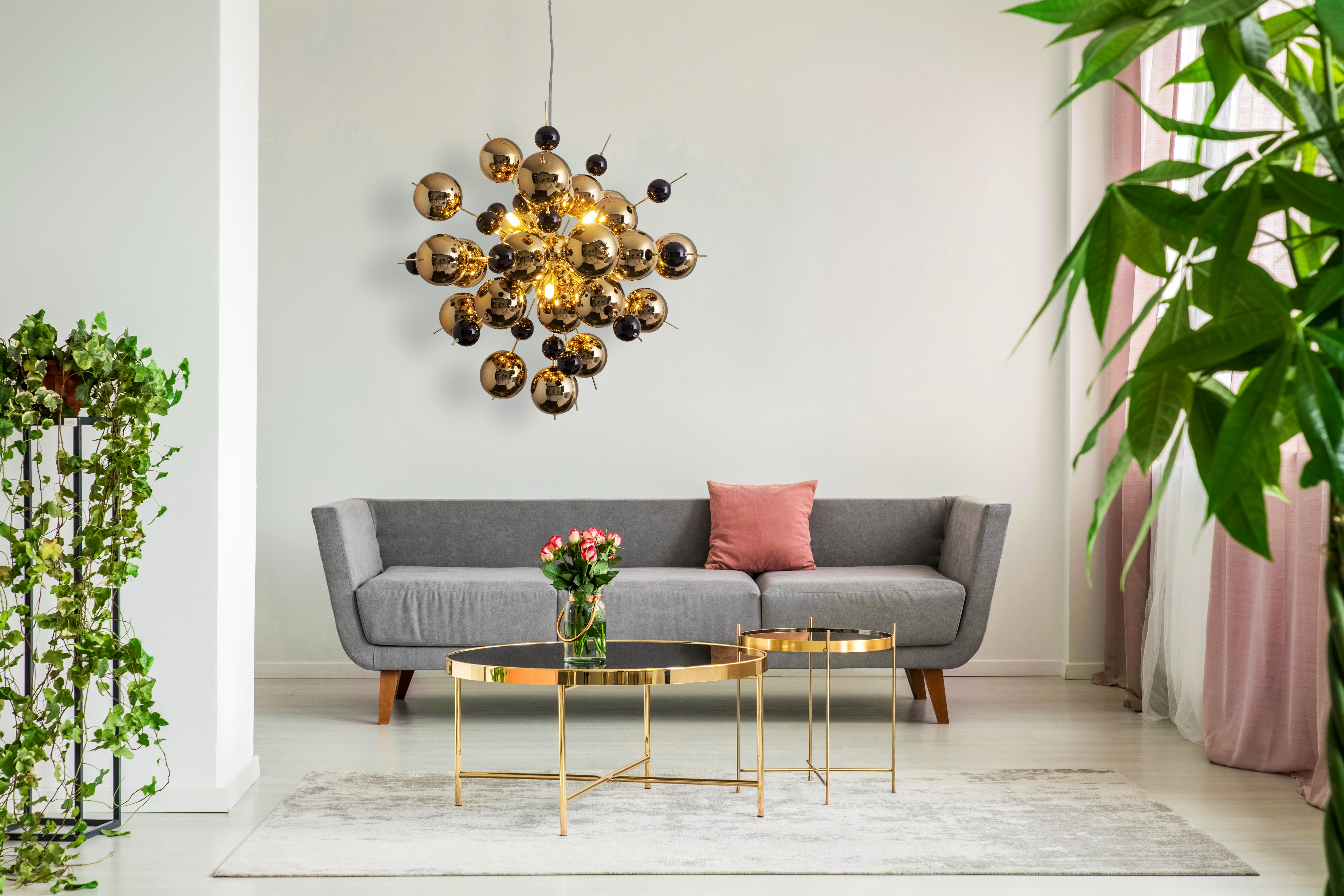 Wohnzimmer mit goldener Deckenleuchte und Sofa. Pflanzen, Couchtisch und Teppich sichtbar.