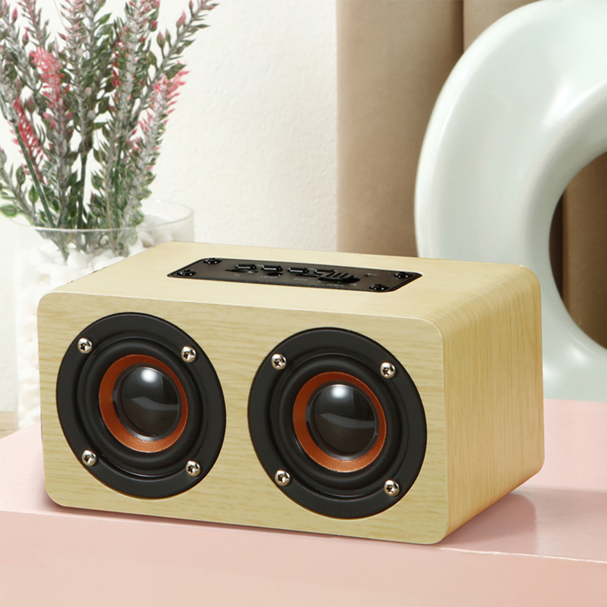 Holzlautsprecher mit zwei schwarzen und orangefarbenen Lautsprechern auf rosa Untergrund.