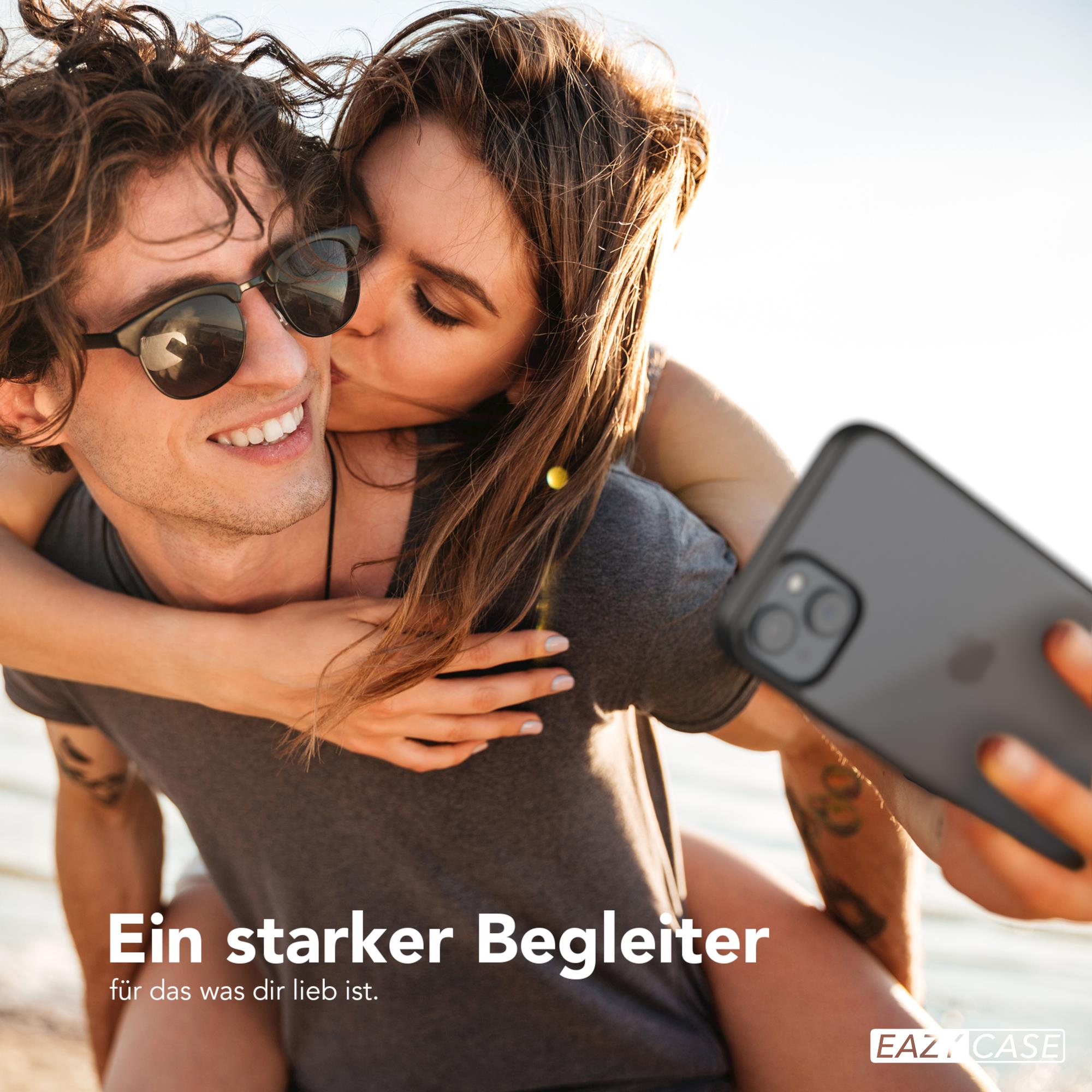 Ein Mann hält ein Telefon und wird von einer Frau auf die Wange geküsst. Hintergrund ist Strand und Himmel.