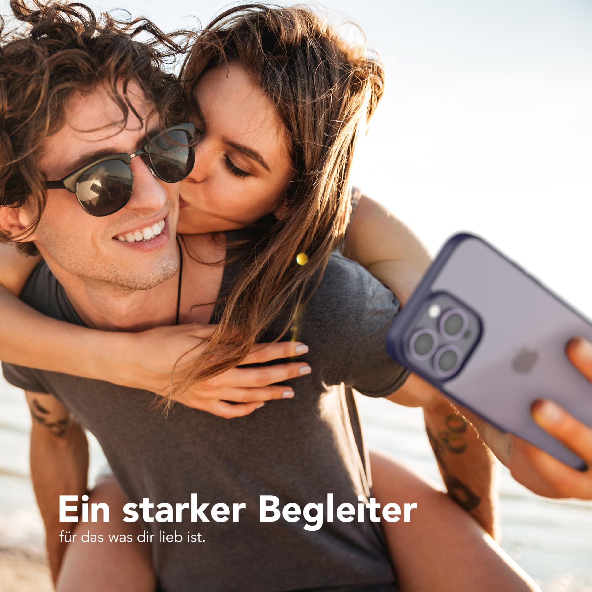 Eine Frau küsst einen Mann auf die Wange. Sie halten ein Telefon. Sonnenuntergang im Hintergrund.