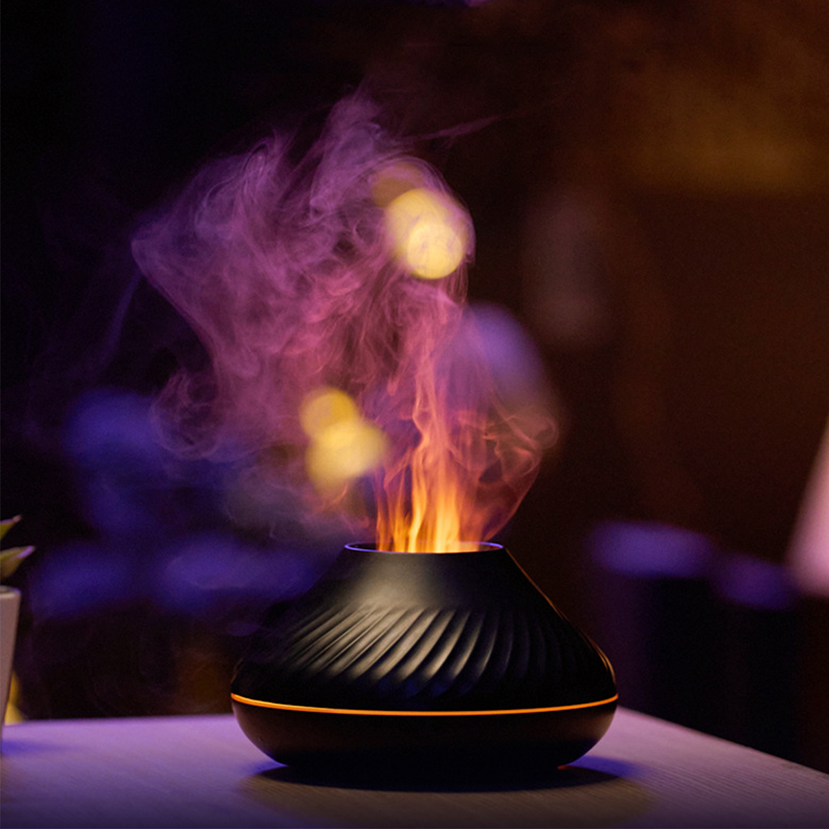 Ein schwarzer Diffusor für ätherische Öle, der flammenartigen Dampf abgibt. Er steht auf einem Tisch.