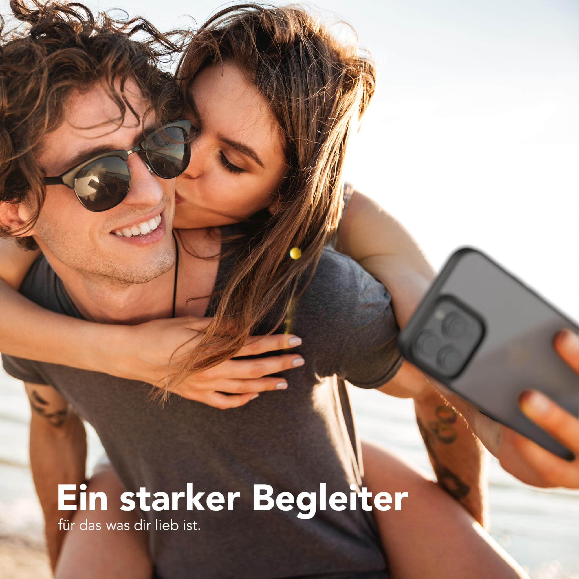 Paar macht Selfie, Frau küsst Mann auf die Wange, sonnige Outdoor-Umgebung.