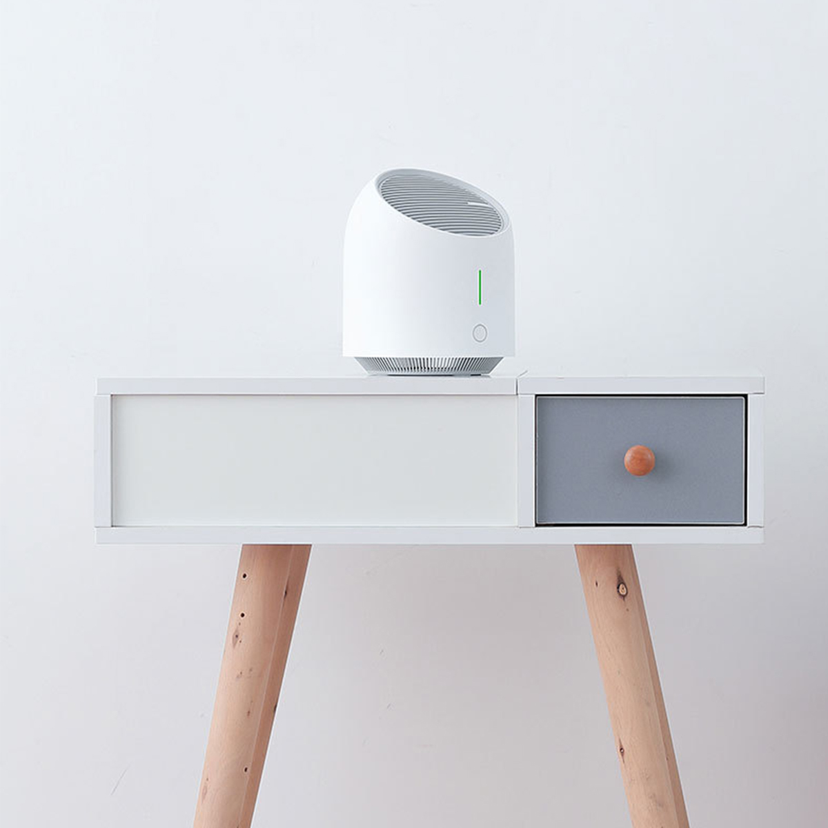 Weißer Luftreiniger auf einem weiß-grauen Schrank mit Holzbeinen. Minimalistisches Design vor einer weißen Wand.