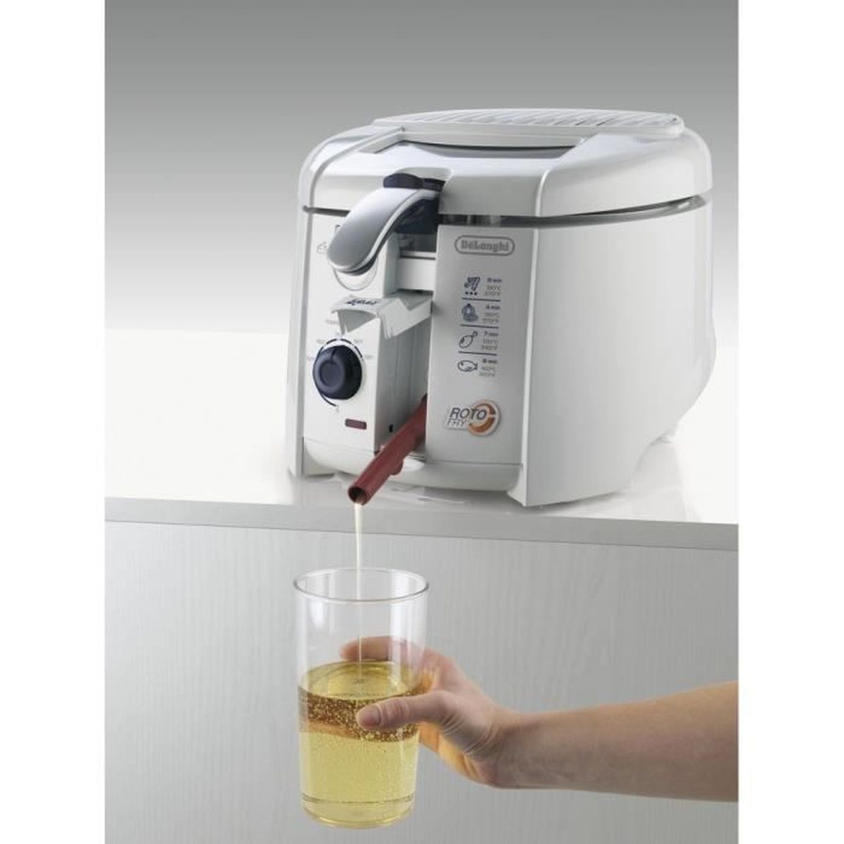 Friteuse giet olie in een glas. Witte machine links, hand rechts.