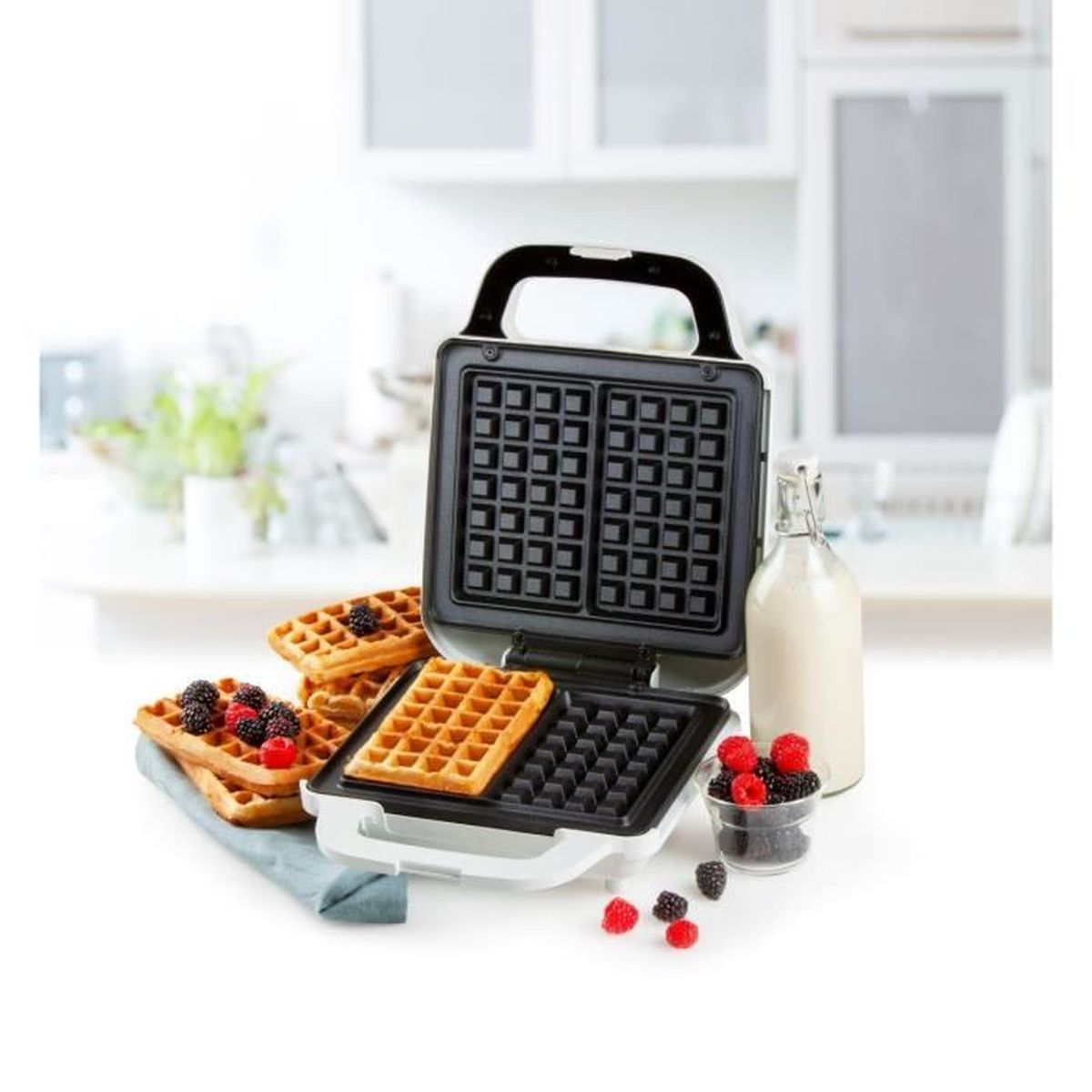Ein Waffeleisen mit Waffeln, Milch und Beeren auf weißem Hintergrund.