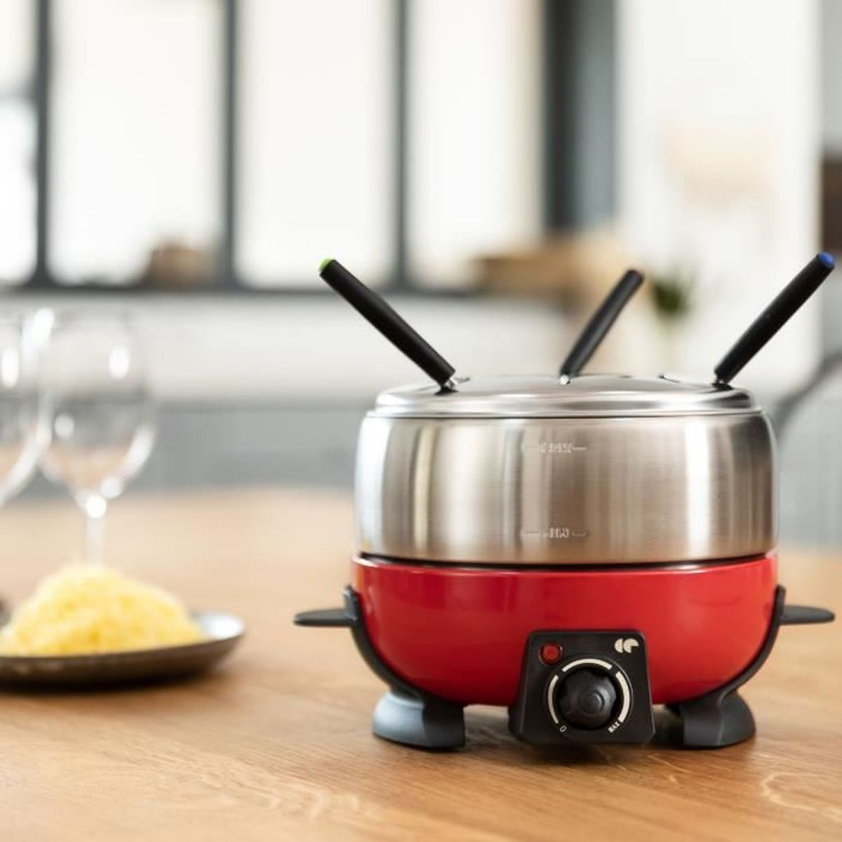 Ein roter Fondue-Topf auf einem Holztisch mit Gabeln und Käse auf einem Teller.