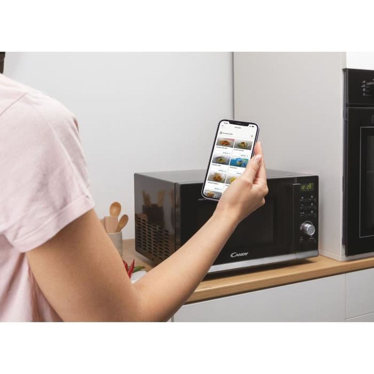 Eine Person steuert eine schwarze Candy-Mikrowelle in einer Küche mit einem Telefon.