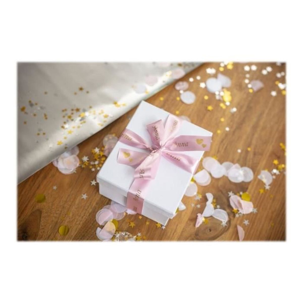 Białe pudełko prezentowe z różową wstążką na drewnianej powierzchni, otoczone konfetti.