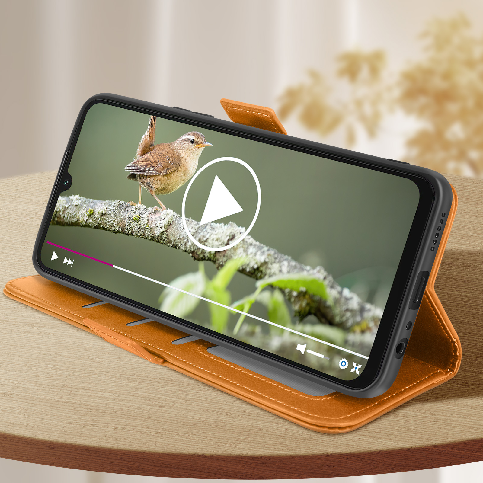 Un telefono in una custodia arancione mostra un video di un uccello su un ramo. Il telefono è su una superficie di legno.