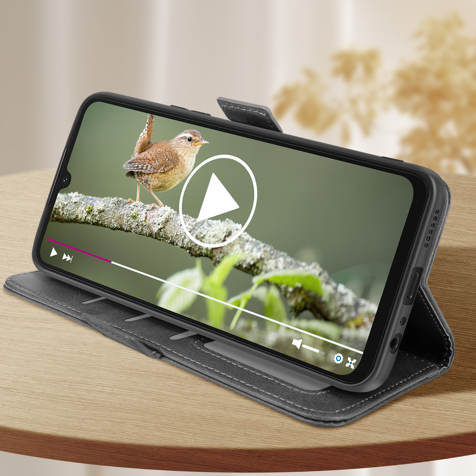 Ein Telefon zeigt ein Video eines Vogels auf einem Ast. Das Telefon befindet sich in einer Hülle auf einem Tisch.