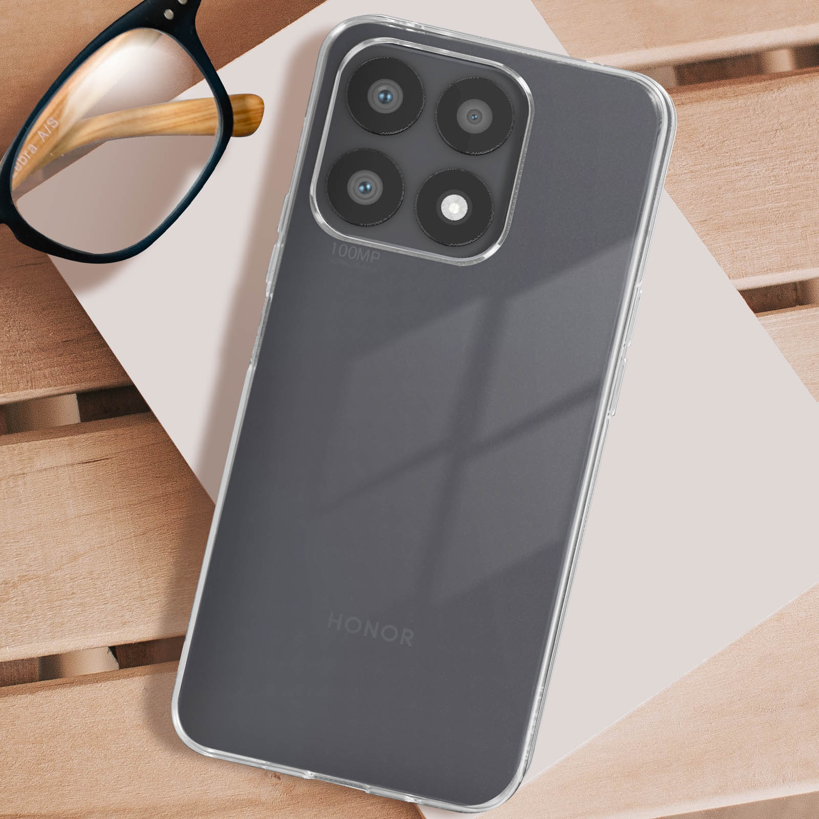 Telefon in klarer Hülle, mit Brille. Telefon hat mehrere Kameras. Auf heller Oberfläche, evtl. Holz.