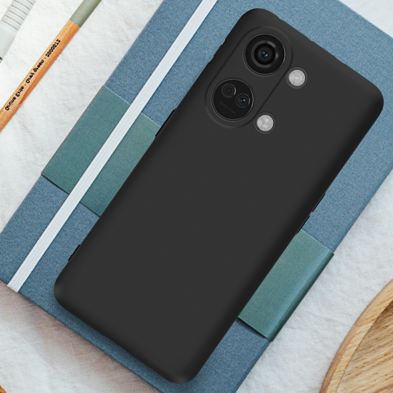 Schwarzes Telefon, zwei Kameras, Triple-Cam-Text, auf Notizbuch, Bleistift daneben.