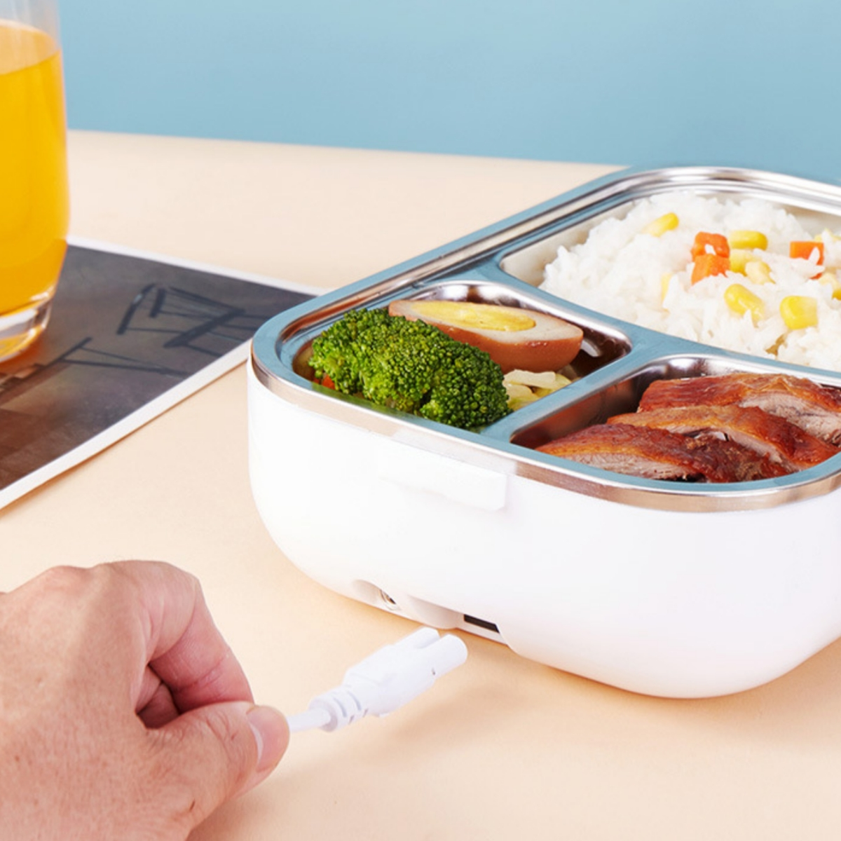 Eine Lunchbox mit Fächern für Lebensmittel, mit einer Hand, die ein weißes Ladegerät einsteckt.