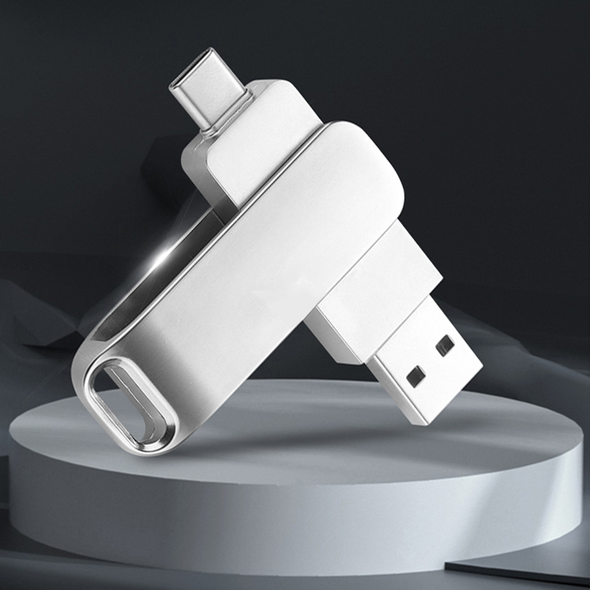 Silberner USB-Stick mit USB-C- und USB-A-Anschluss. Er steht auf einem weißen Sockel mit dunklem Hintergrund.