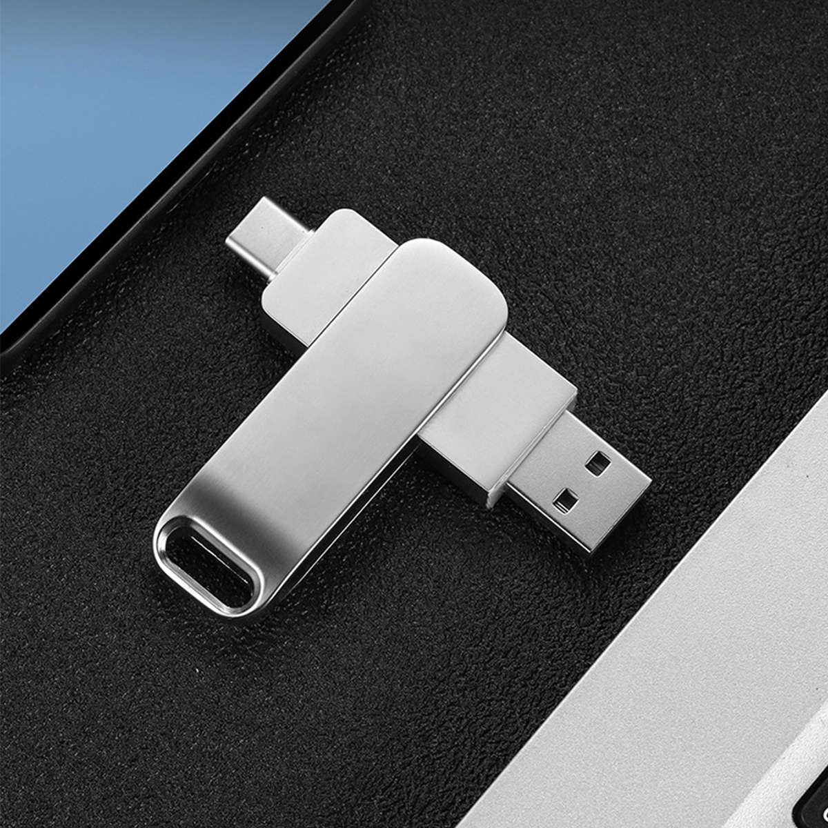 Silberner USB-Stick mit einem USB-A- und USB-C-Anschluss. Er liegt auf einer schwarzen Lederoberfläche.