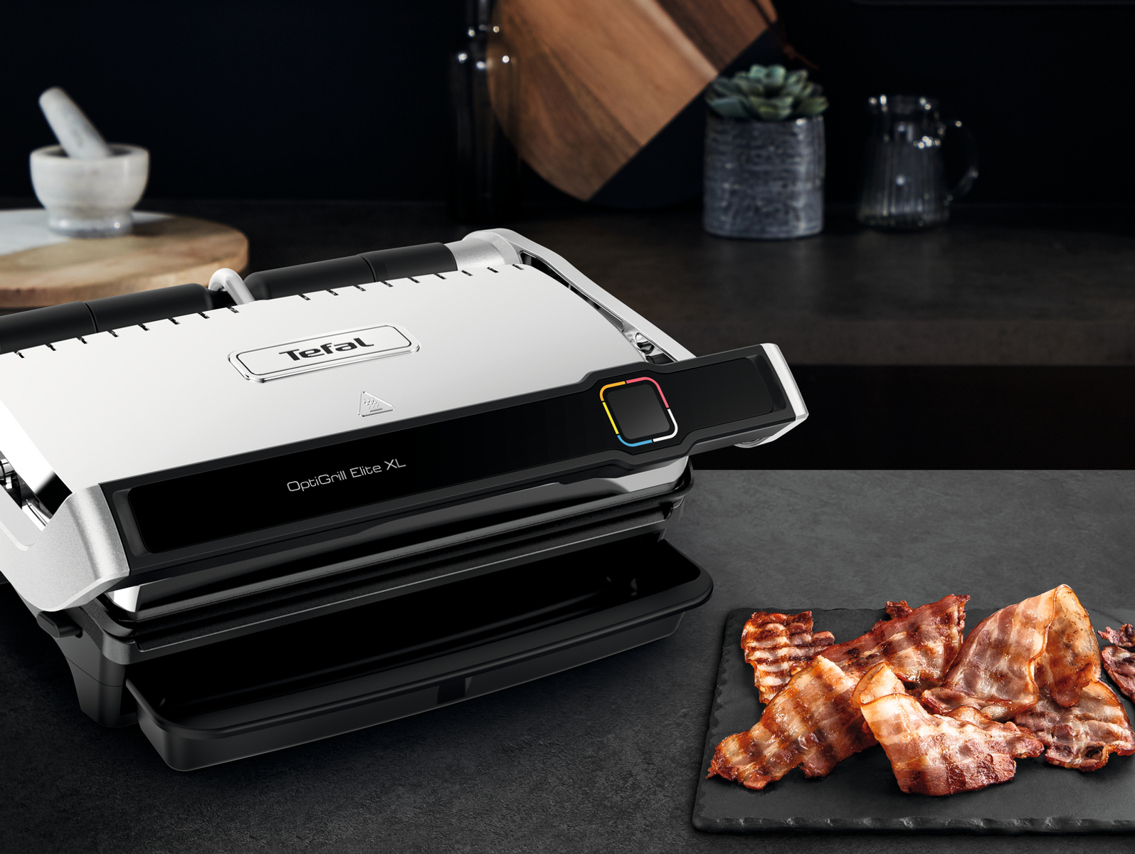 Tefal OptiGrill Elite XL auf dunkler Oberfläche, mit Speck. Eine Küchenszene.