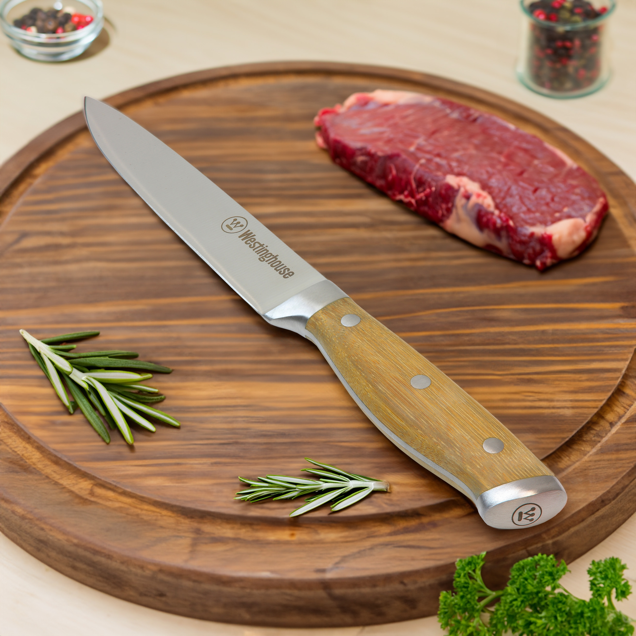Ein Messer auf einem hölzernen Schneidebrett mit einem Stück Steak und Rosmarin. Es gibt Pfefferkörner in Gläsern.